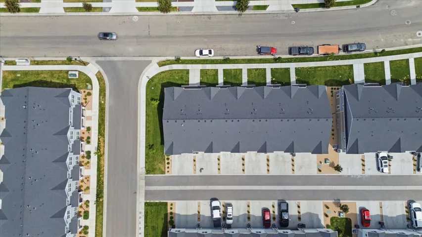 Residential development featuring multiple townhome-style buildings with dark gray shingle roofs, individual concrete driveways, and landscaped green spaces