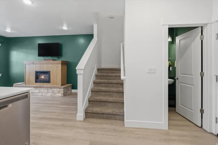 Carpeted staircase with white balustrade, wood-finish flooring, and a fireplace featuring a stone base and wood-finish surround