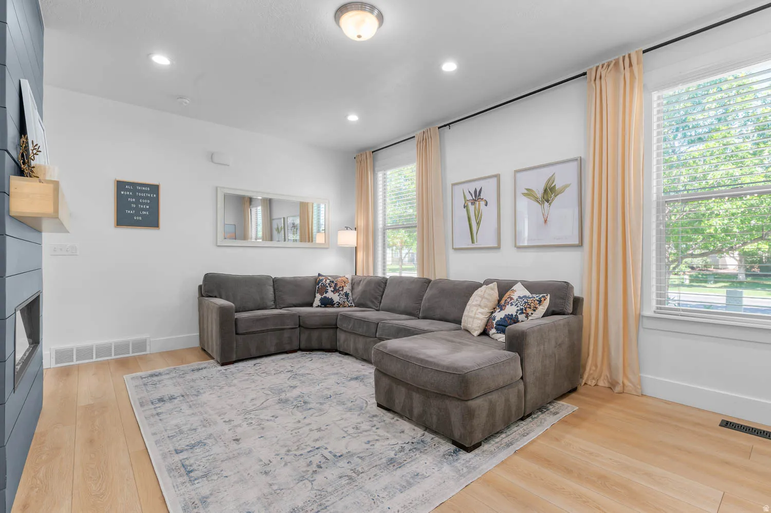 Spacious living area featuring light wood-finish flooring, recessed lighting, and large windows with blinds