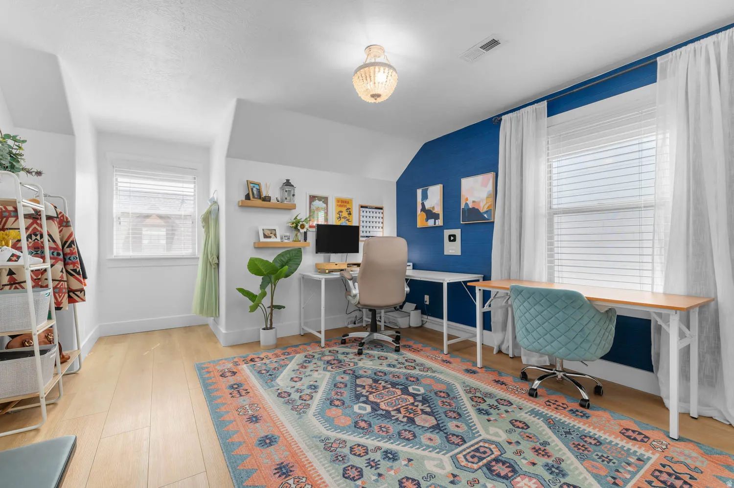 Bright room featuring wood-finish flooring, multiple windows with blinds, built-in shelving, and a decorative ceiling light fixture