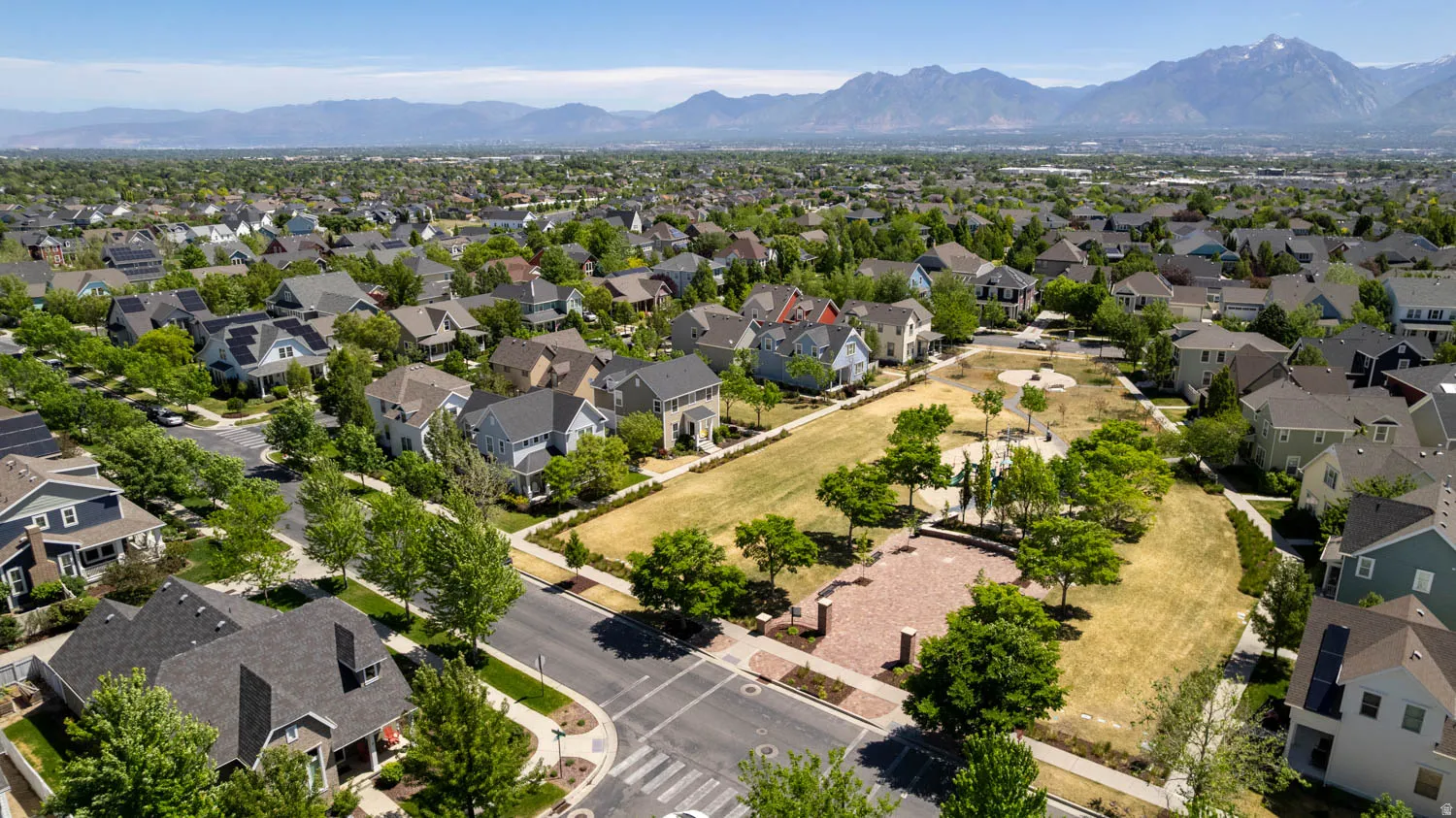 Expansive aerial view showcasing a neighborhood with diverse residential architecture and a prominent central green space