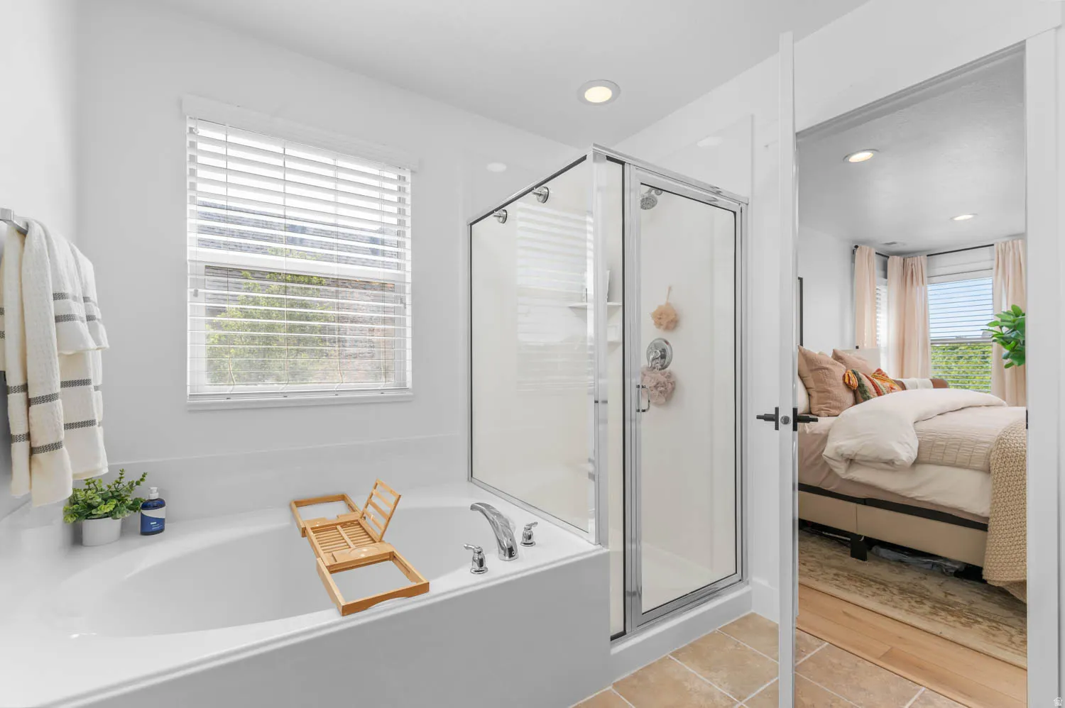 White soaking tub with chrome fixtures, an adjacent glass-enclosed shower, and a privacy window with horizontal blinds