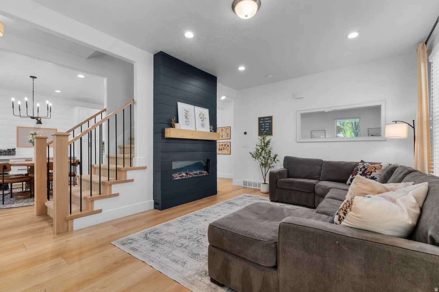 Living area featuring wood-finish flooring, a contemporary fireplace with an integrated mantel, a contrasting shiplap accent wall, and recessed ceiling lighting