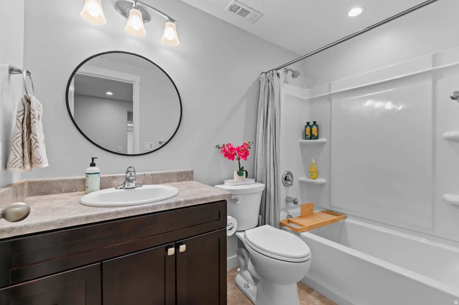 Bathroom featuring a dark wood vanity with a light countertop, an oval-framed mirror, and a white integrated sink