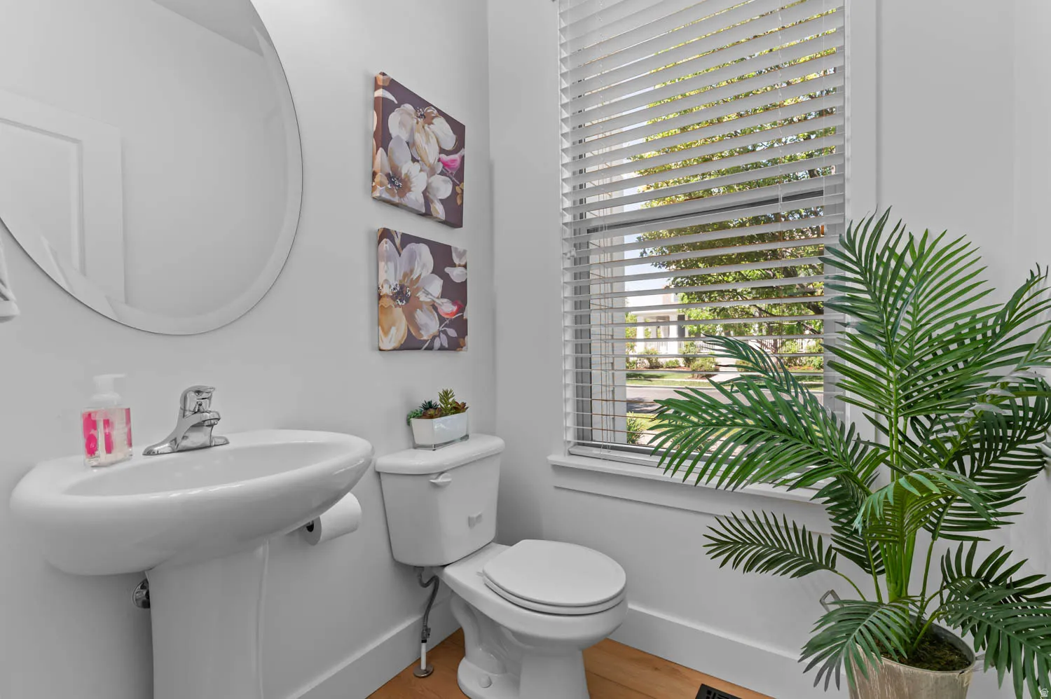 Pedestal sink with chrome faucet, complemented by a round wall-mounted mirror