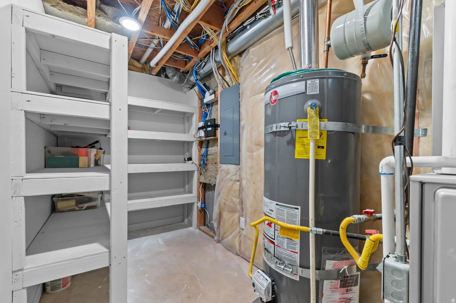 Utility space featuring a water heater, electrical panel, and exposed ceiling joists with wiring