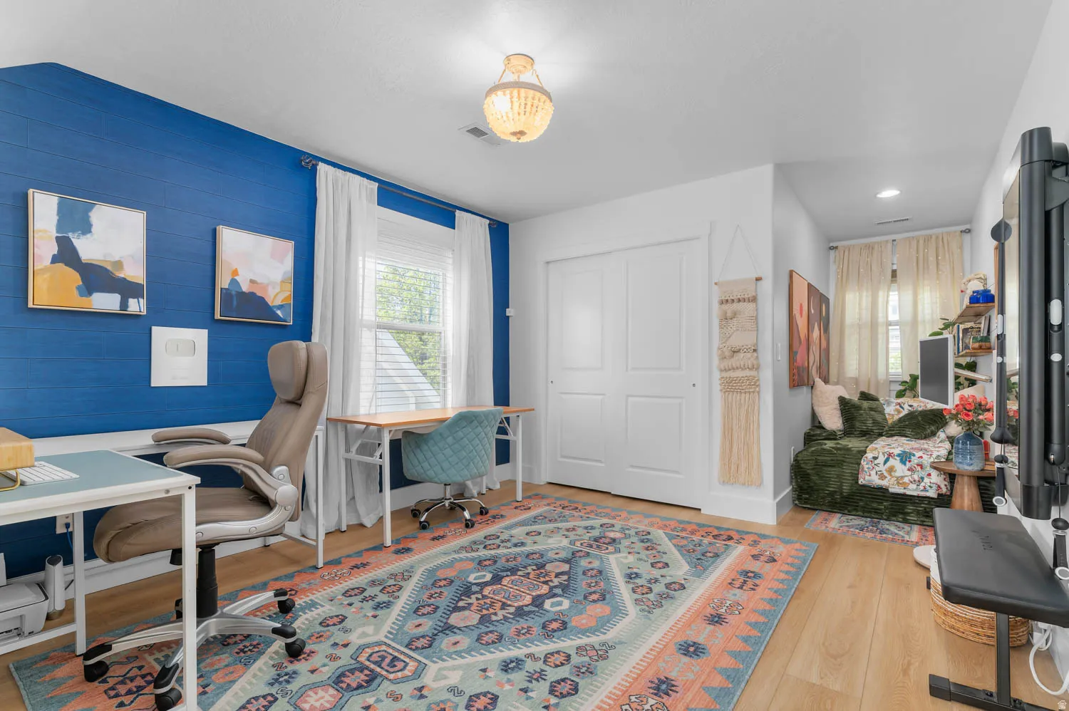 Accent wall with blue textured wallpaper, light wood-finish flooring, white double bi-fold closet doors, recessed lighting, and a decorative ceiling fixture