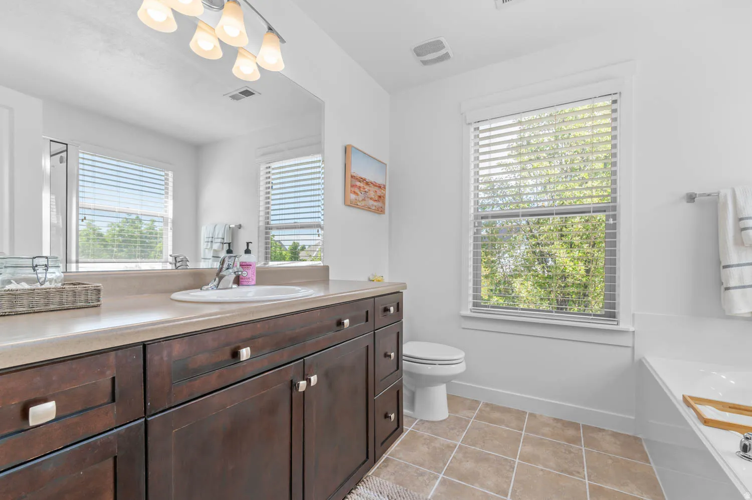 Bathroom featuring a wood-finish vanity with a single basin sink, a large mirror, and a window with horizontal blinds