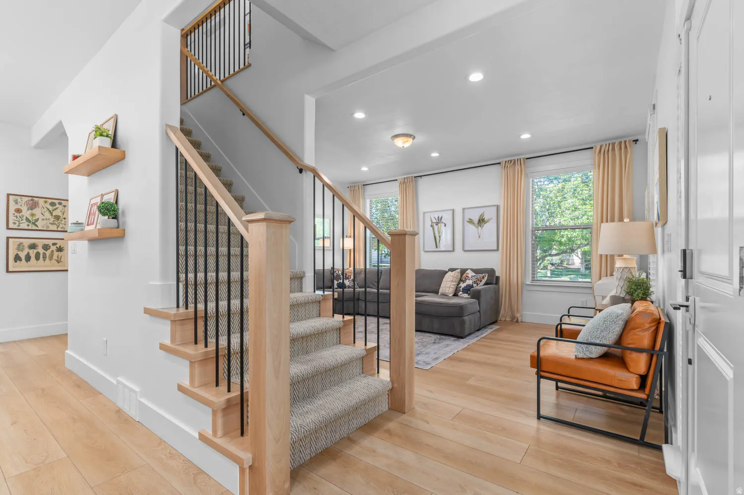 Open-concept entryway featuring wood-finish flooring, a carpeted staircase with wood newel posts and black iron balusters, recessed lighting, and white walls