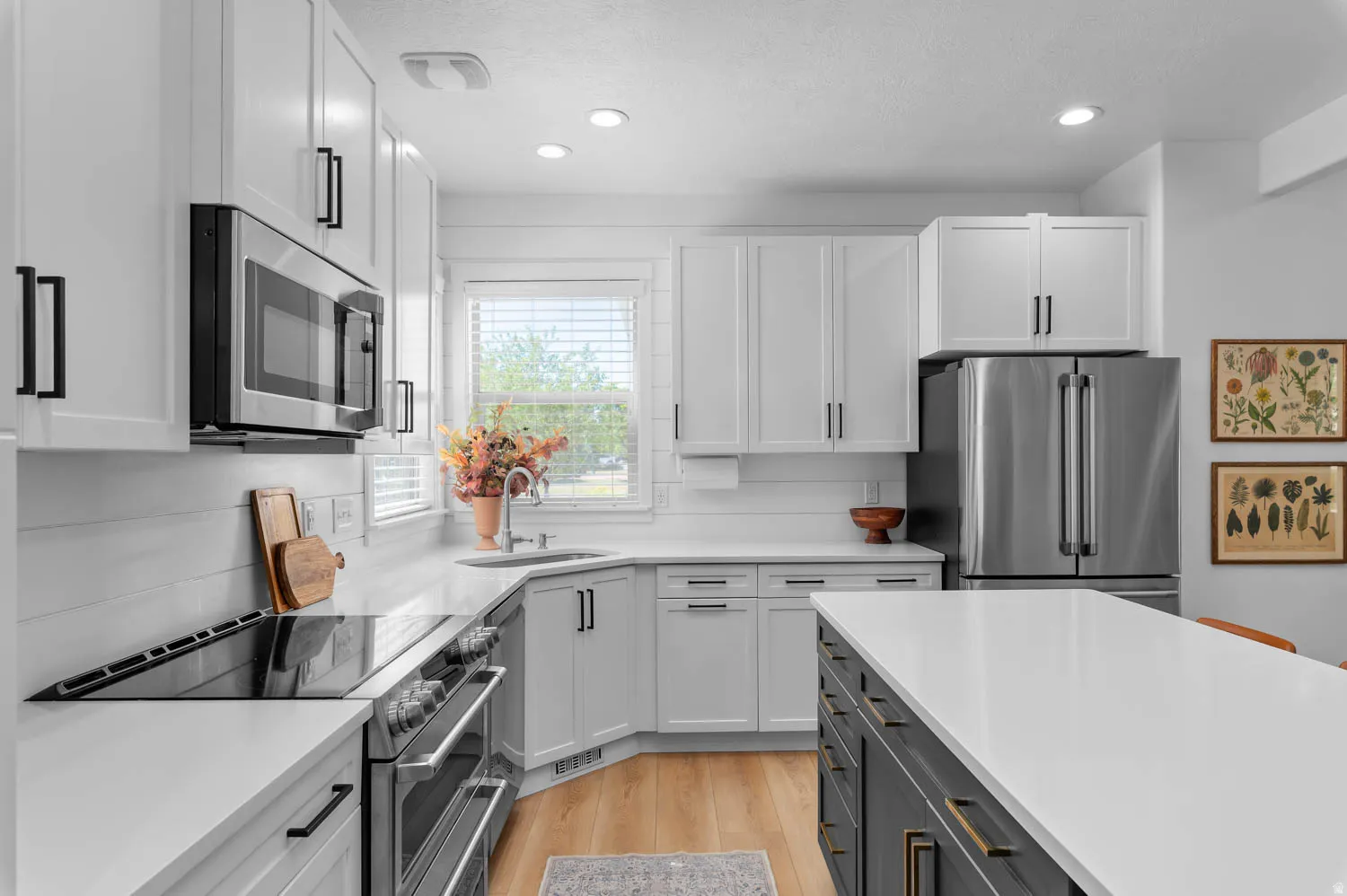 Modern kitchen featuring white shaker cabinetry, stainless steel appliances, light wood-finish flooring, and a central island with white countertop