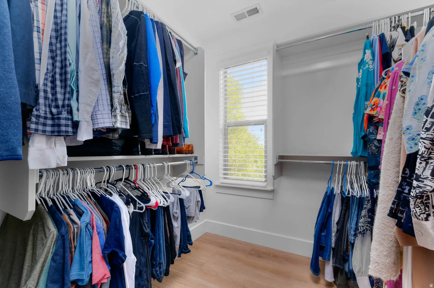 Walk-in closet featuring light wood-finish flooring, white walls, and a window with blinds