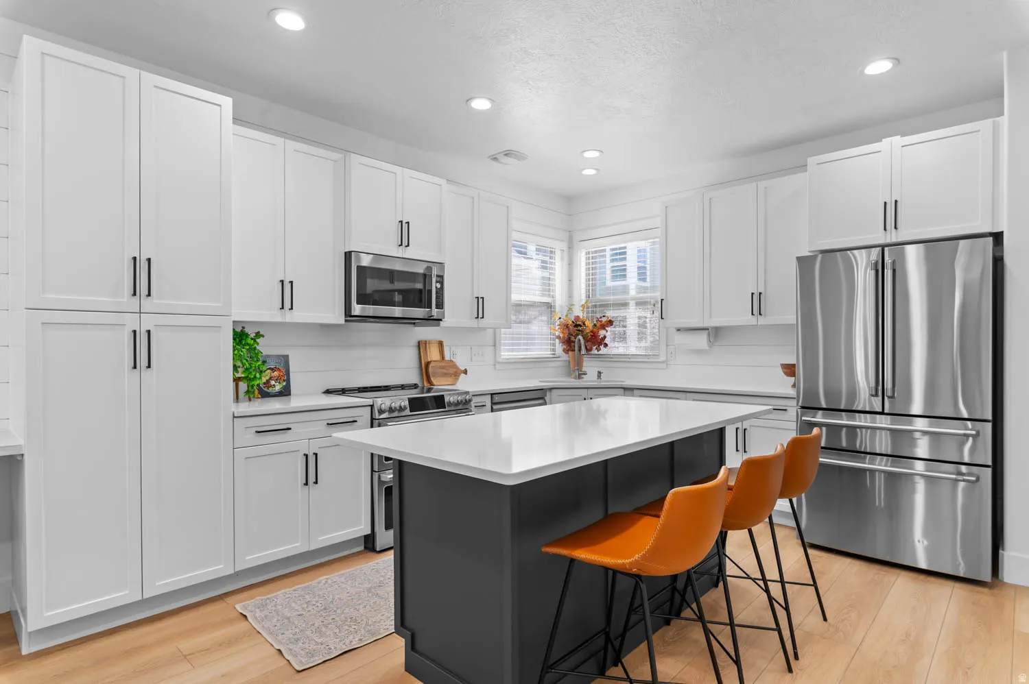 Modern kitchen featuring white shaker cabinetry with matte black hardware, stainless steel appliances, a center island with a white countertop and dark gray base, light wood-finish flooring, and recessed lighting