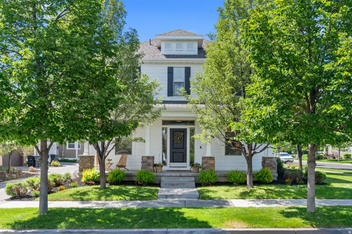 Traditional-style residence featuring white siding, a prominent front porch with white columns and stone bases, a dark entry door, and dark shutters