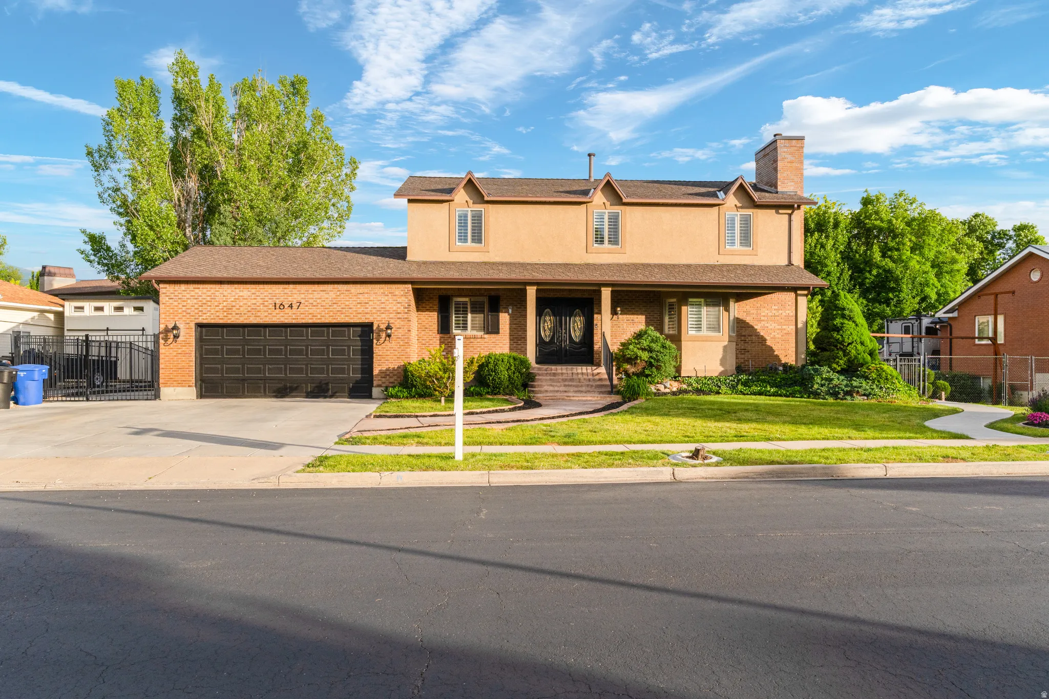Two-story residence featuring a brick and stucco facade, a two-car garage with a dark panel door, and a covered front porch with double entry doors