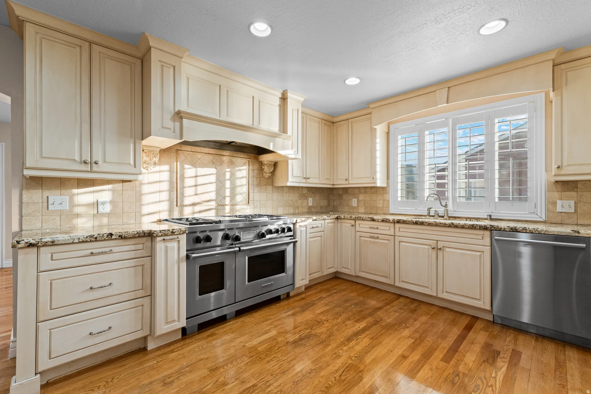 Gourmet kitchen featuring extensive cabinetry, stainless steel appliances, granite countertops, a tiled backsplash, and wood-finish flooring