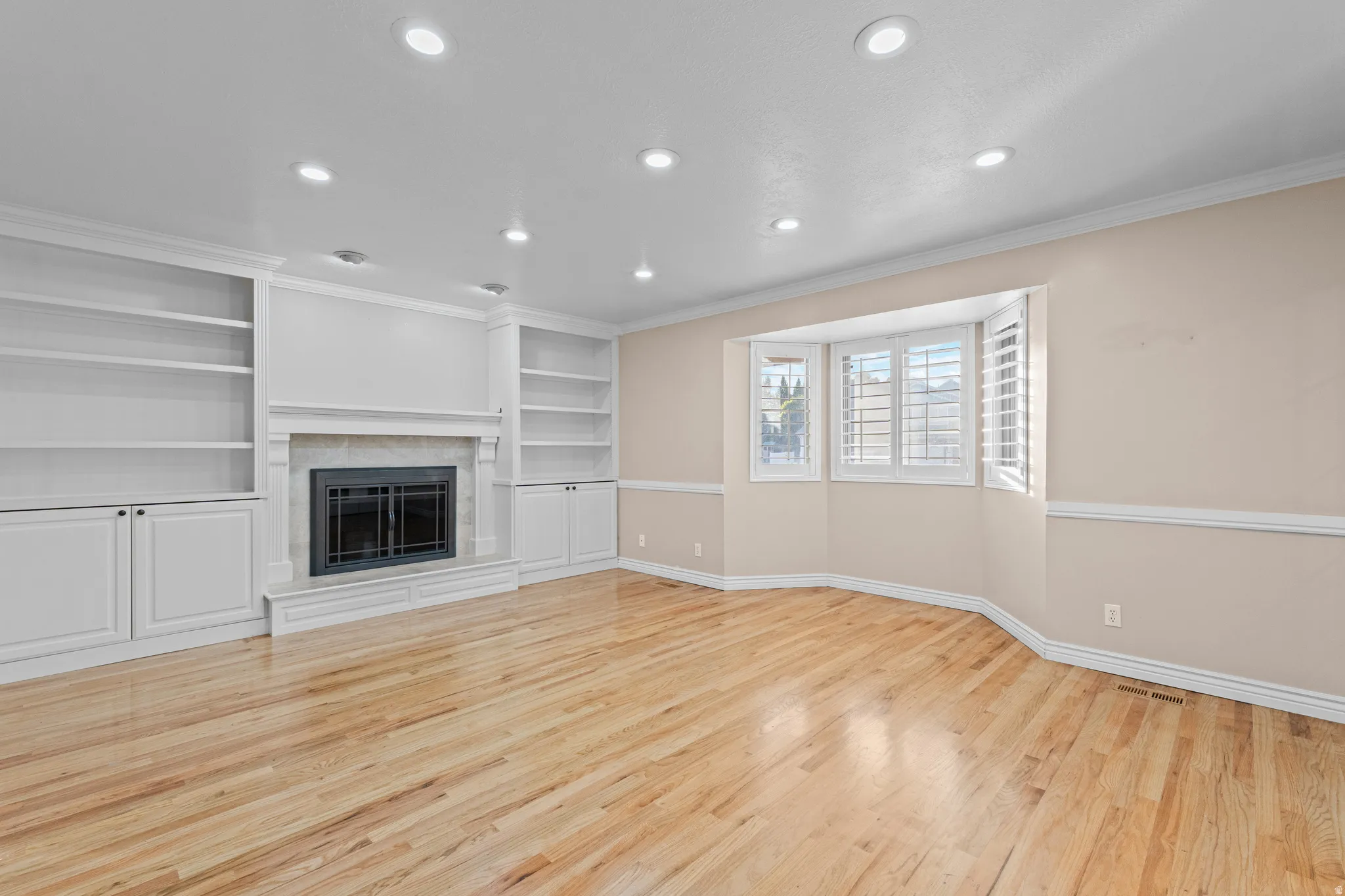 Living area featuring wide plank wood-finish flooring, recessed lighting, and a bay window with plantation shutters