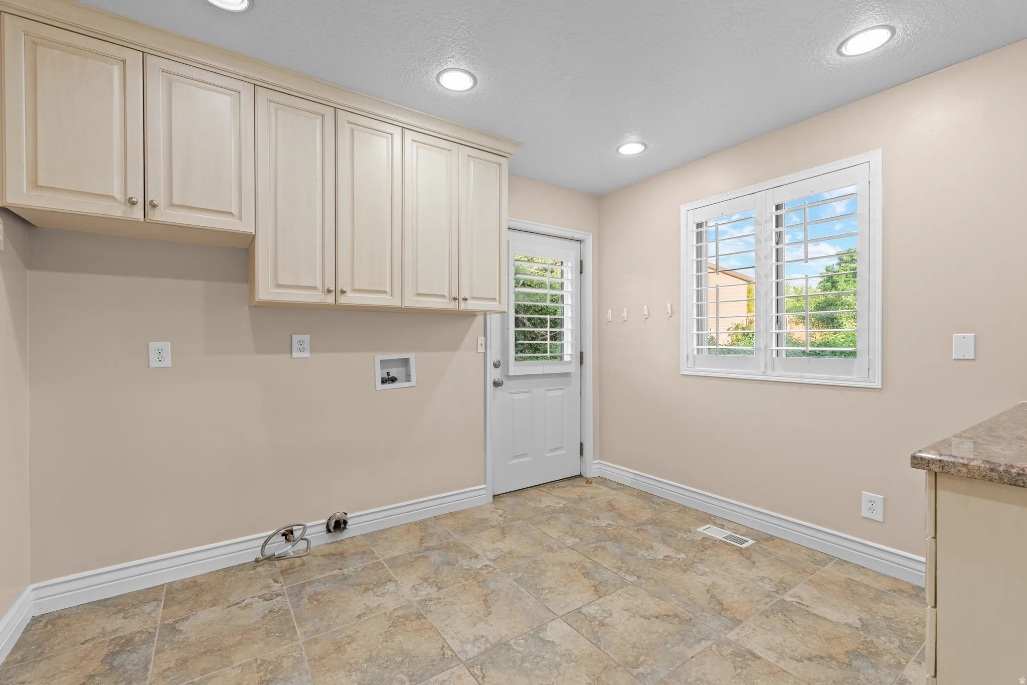 Utility room featuring tile flooring, abundant cabinetry, recessed lighting, and a window with plantation shutters