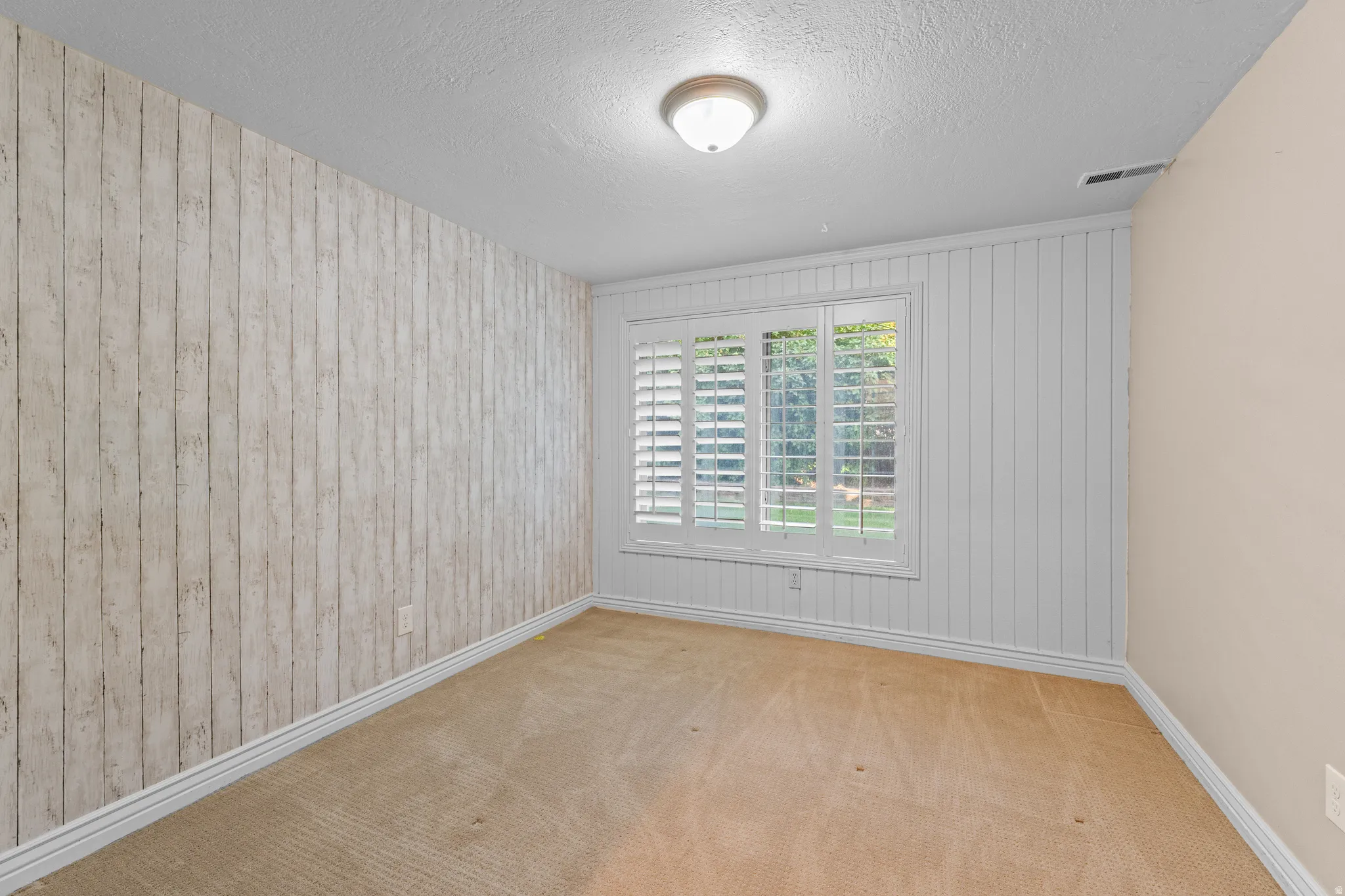Room featuring a window with white louvered shutters, light beige carpeting, and a ceiling-mounted light fixture