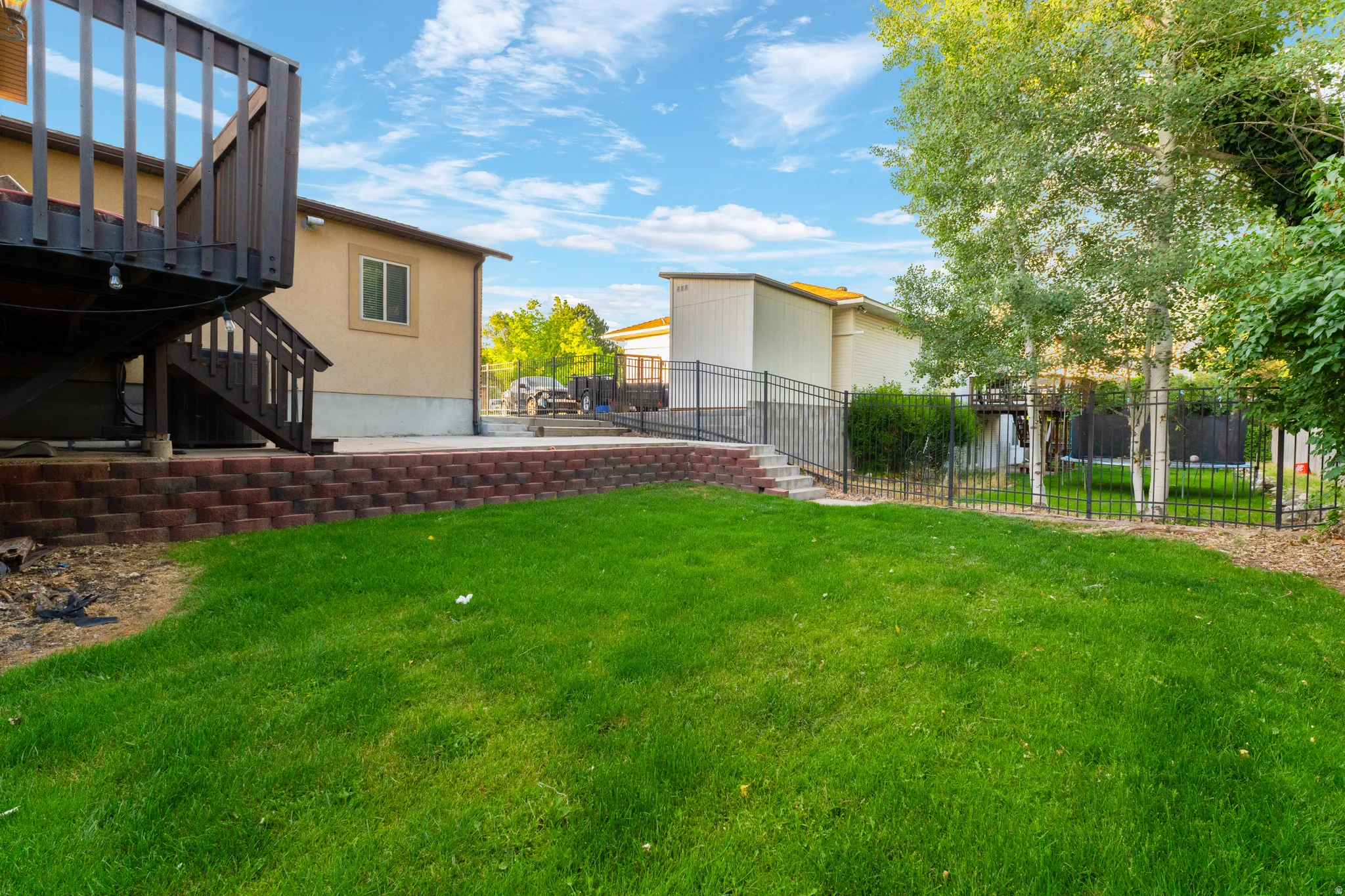 Expansive backyard featuring a manicured lawn, mature trees, and a black wrought-iron fence
