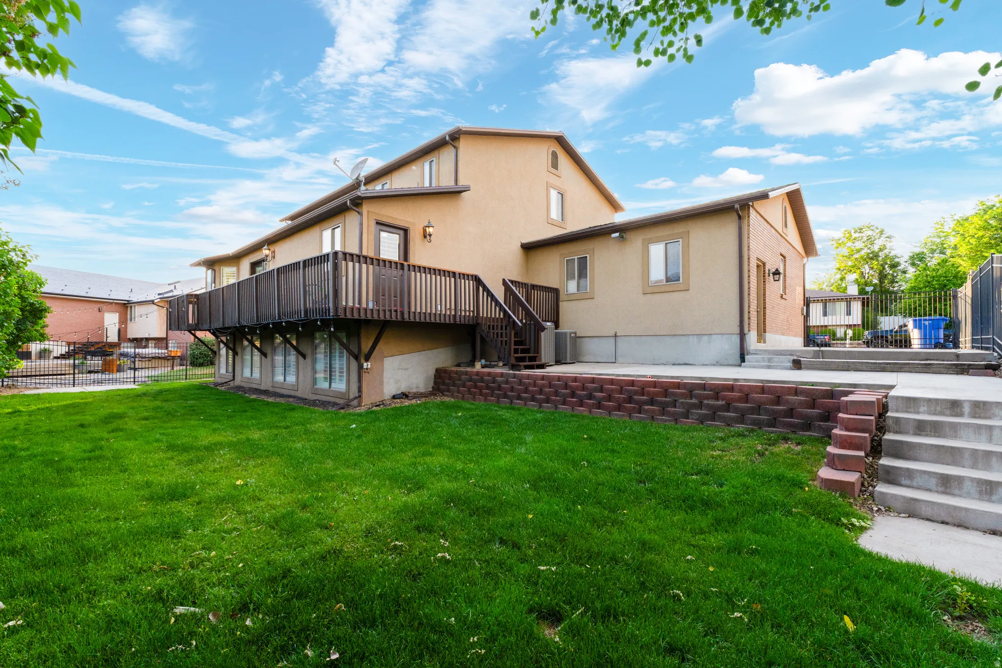 Expansive backyard featuring a manicured lawn, multi-level patio, and a raised wood deck with staircase access