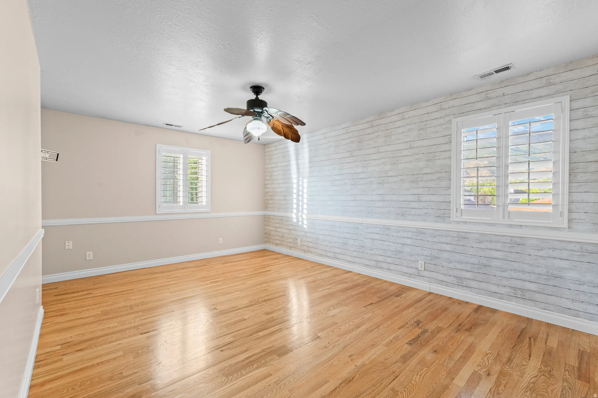 Spacious room featuring wood-finish flooring, a ceiling fan with integrated lighting, and white plantation shutters