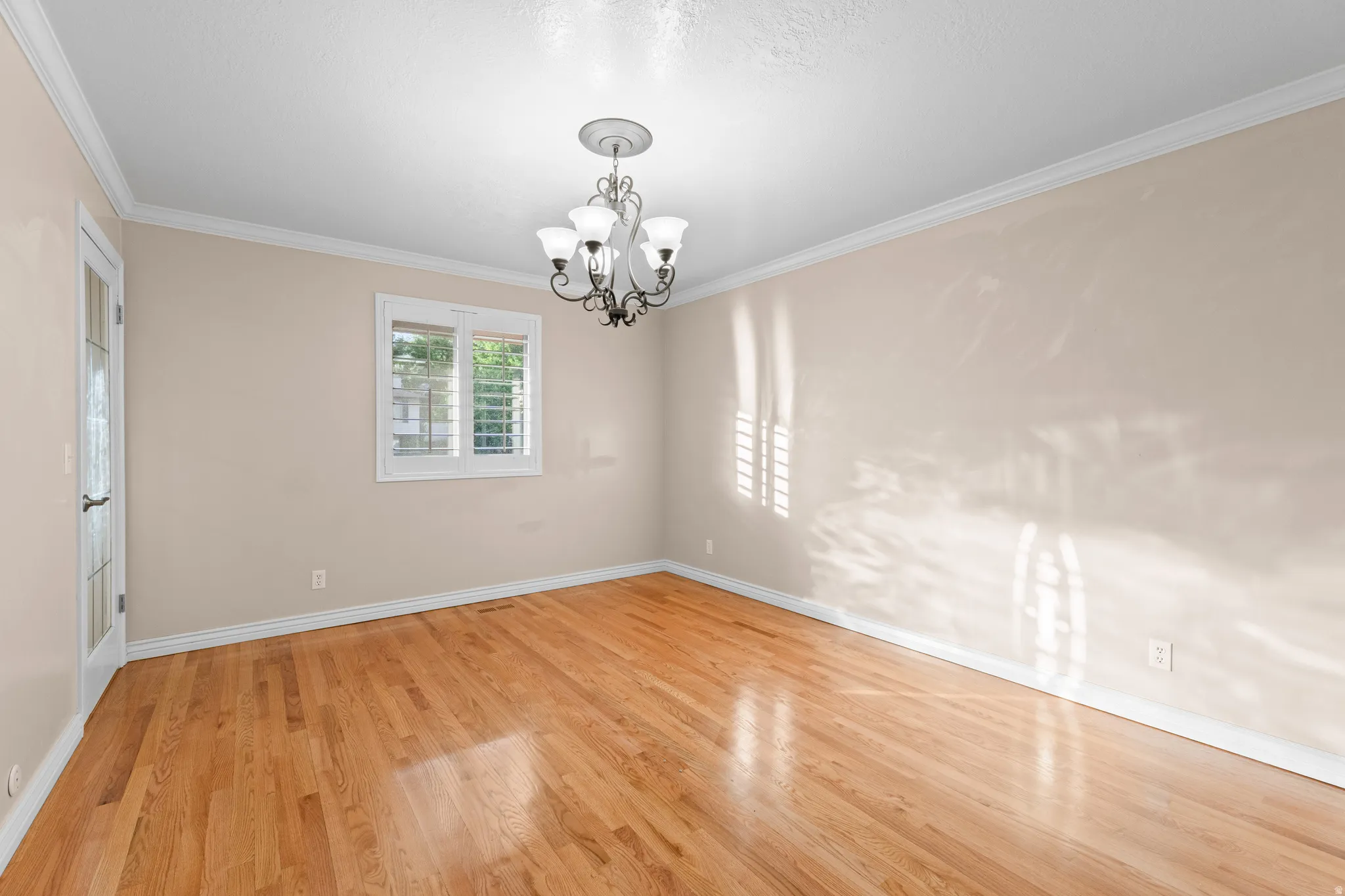 Hardwood flooring extending throughout the room, crown molding, and a chandelier lighting fixture
