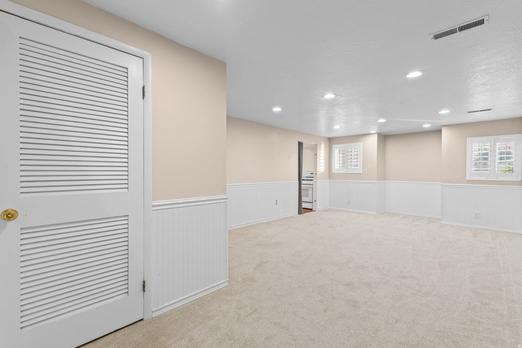 Spacious room featuring neutral carpeting, recessed lighting, and wainscoting paneling