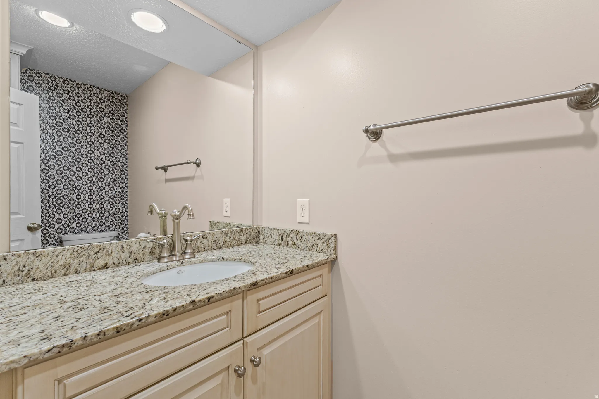 Bathroom vanity featuring a speckled countertop, undermount sink, and brushed nickel faucet