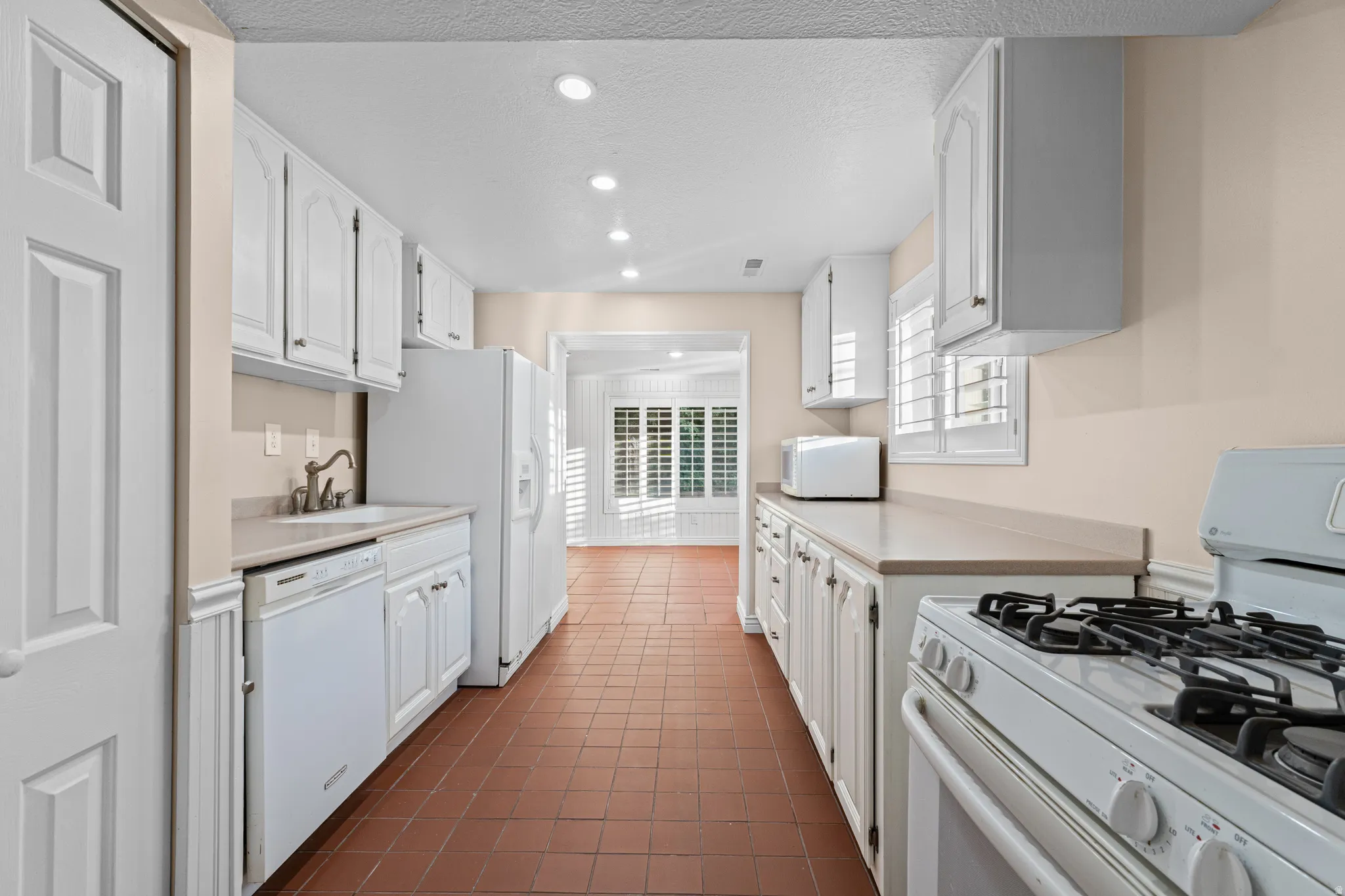 Galley kitchen featuring white cabinetry, light-toned countertops, and a full suite of white appliances