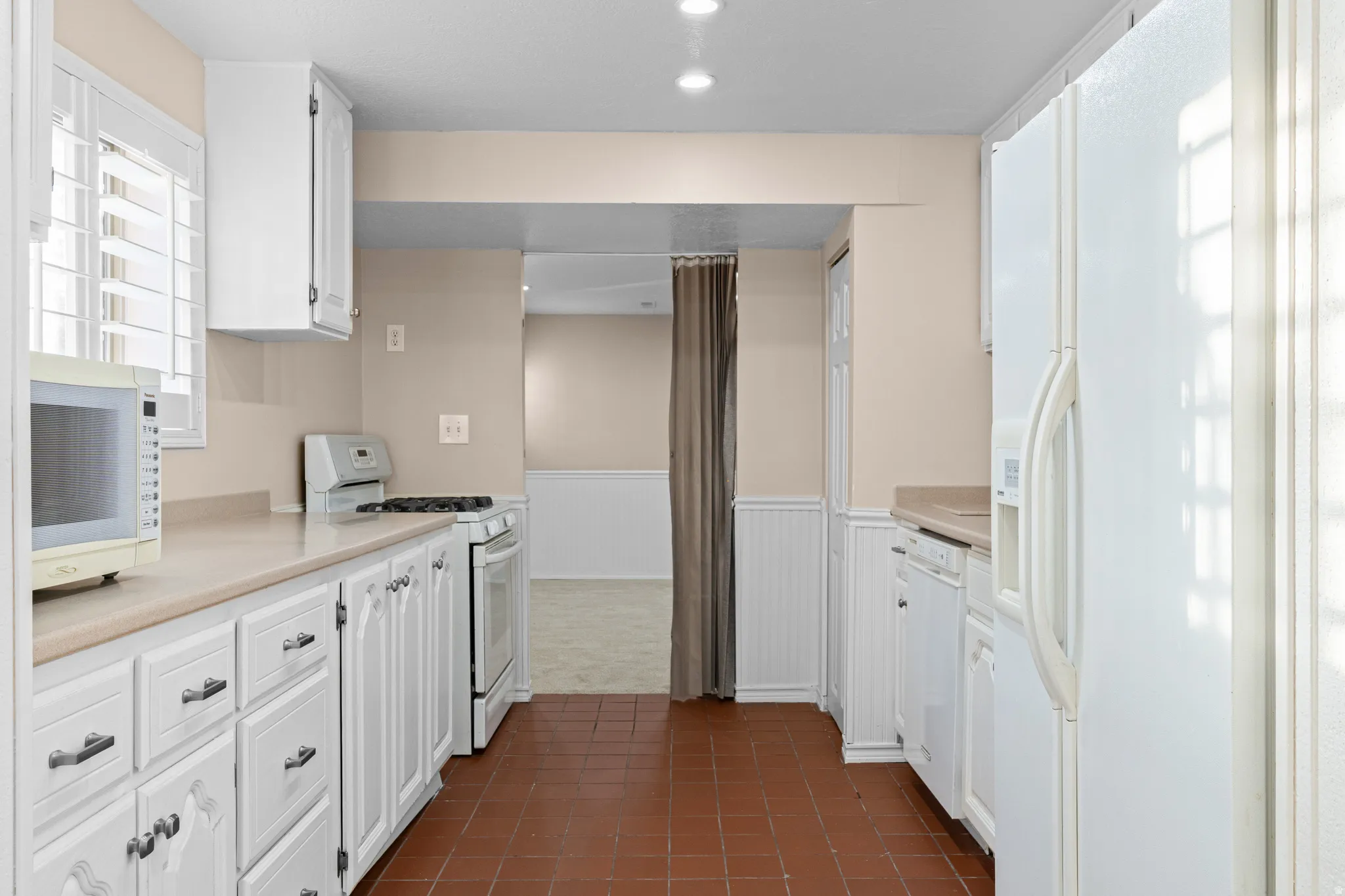 Kitchen featuring white cabinetry, light-toned countertops, a white gas range, and terracotta tile flooring