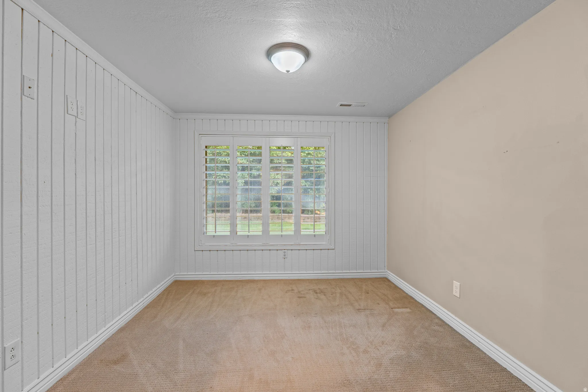 Room with neutral carpeting, white wainscoting, and a window featuring white plantation shutters