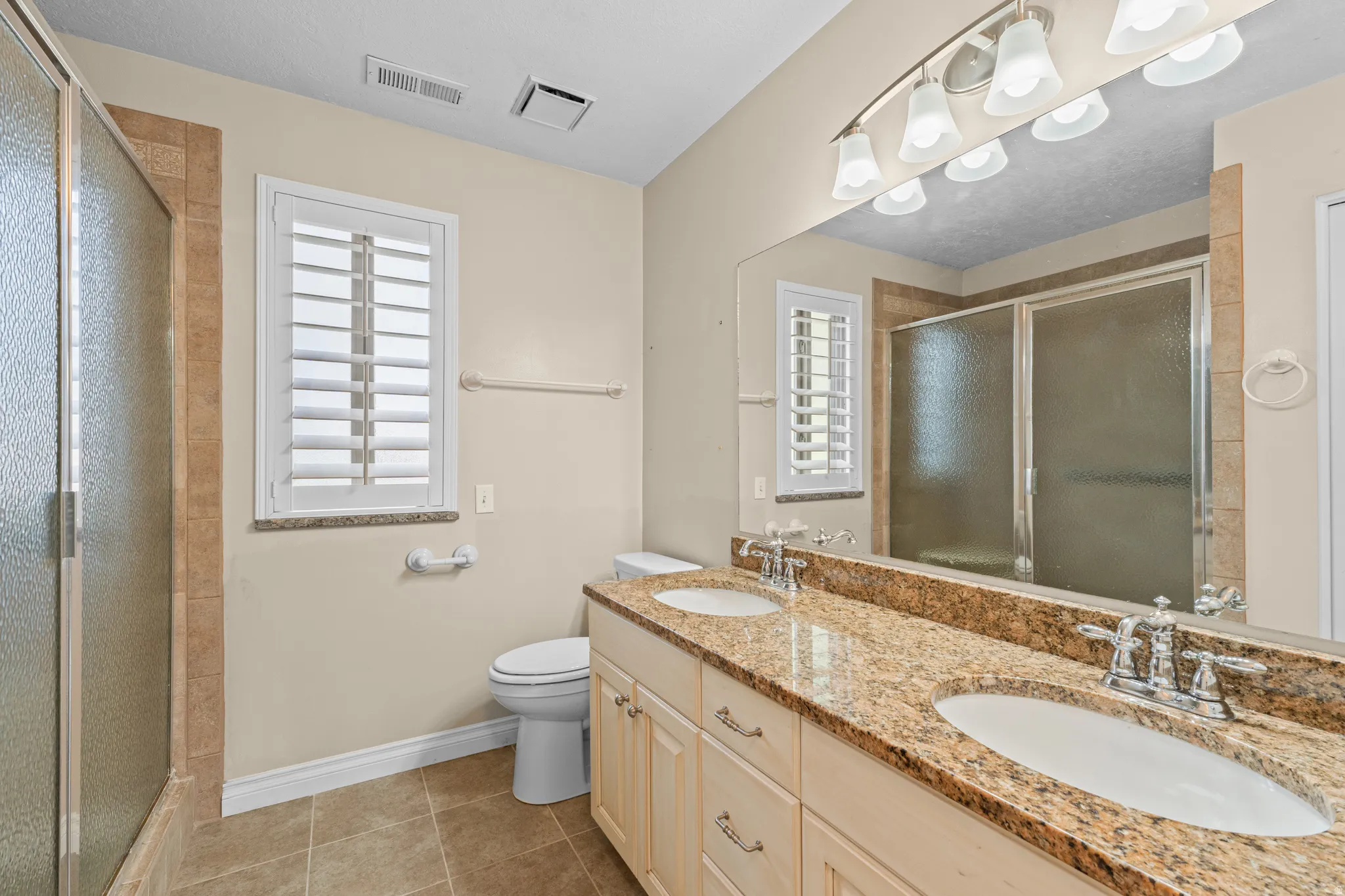 Dual sink vanity with a natural stone countertop, wood-finish cabinetry, and chrome fixtures