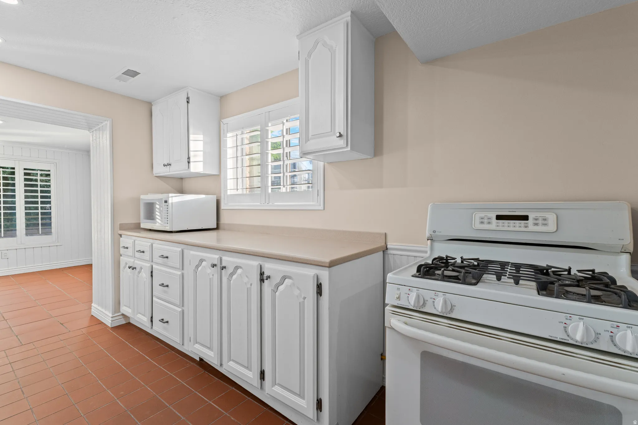Kitchen featuring a white gas range, white cabinetry with dark hardware, solid surface countertops, and terracotta tile flooring