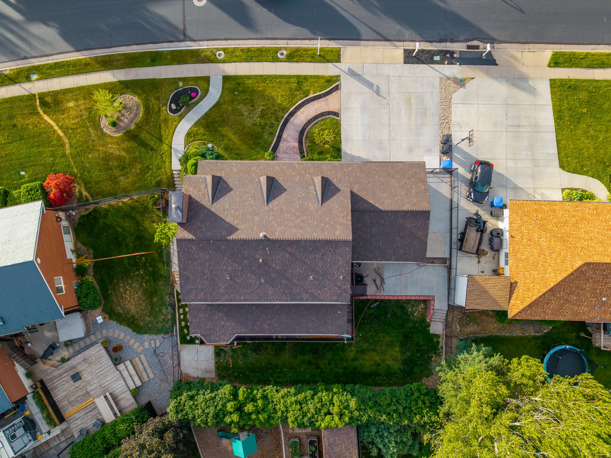 Aerial perspective showcasing a property with a brown shingle roof, multiple dormer windows, and a concrete driveway