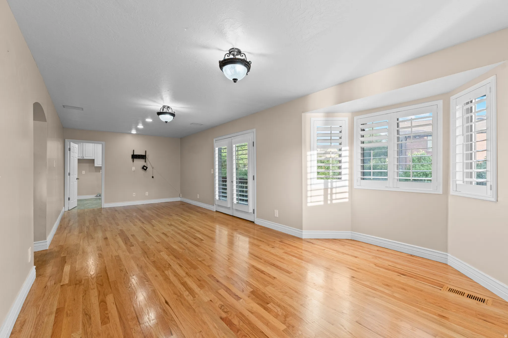 Spacious room featuring wood-finish flooring, bay windows with plantation shutters, double French doors, and recessed lighting