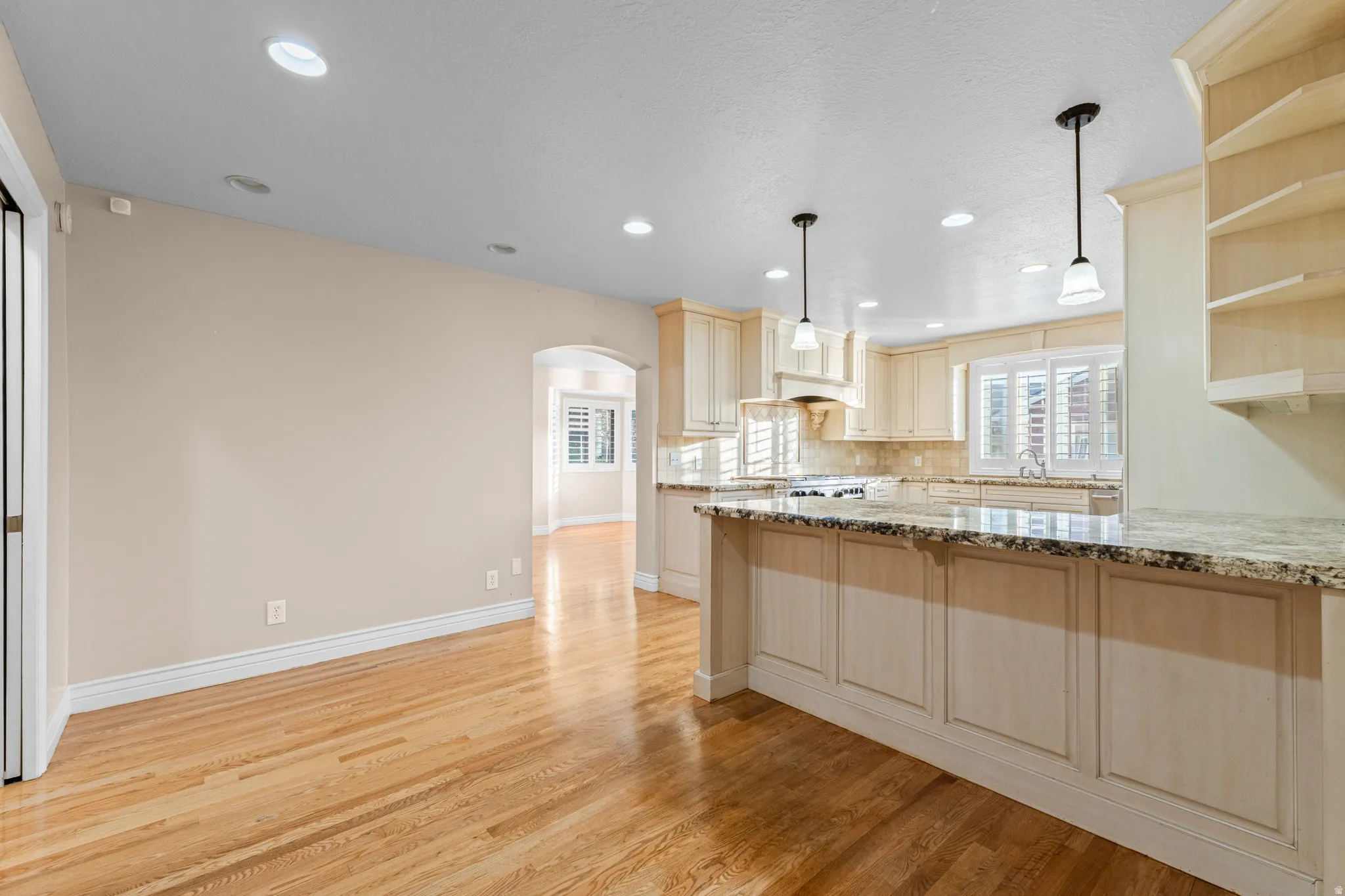 Open-concept kitchen featuring light-toned cabinetry, granite countertops, and hardwood flooring