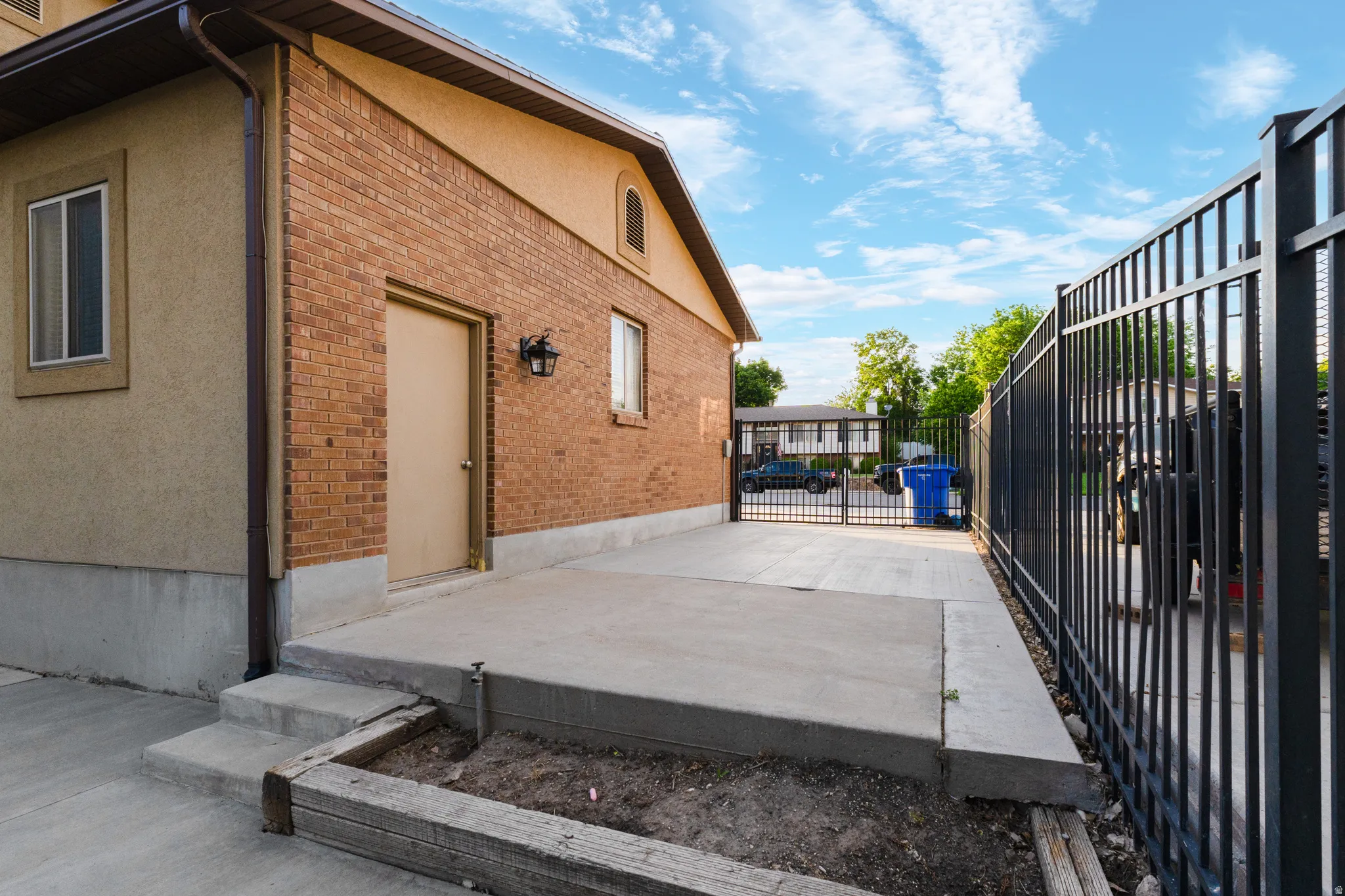 Exterior featuring brick and stucco siding, a concrete patio, and a black wrought iron fence