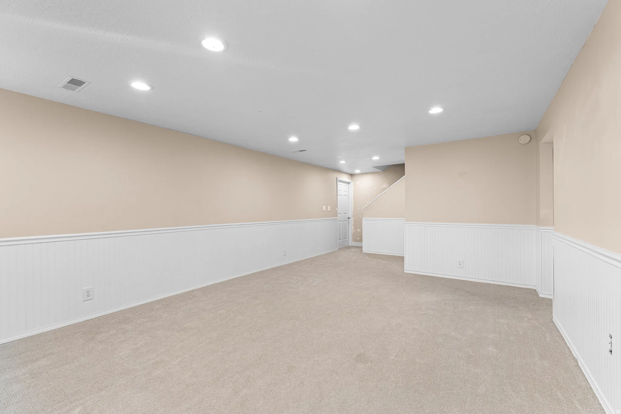Spacious room featuring neutral carpeting, light beige walls, and white wainscoting