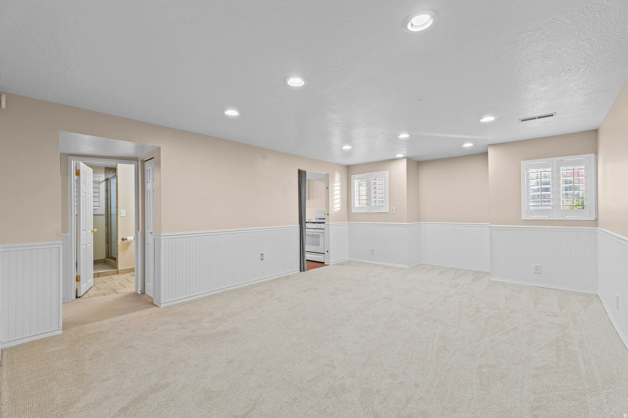 Spacious carpeted room featuring recessed lighting, two windows with white plantation shutters, and beadboard wainscoting
