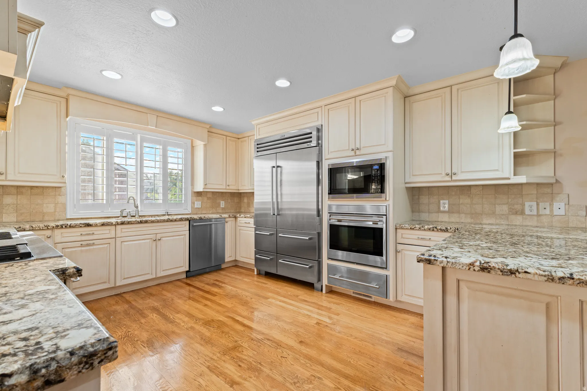 Kitchen featuring light wood cabinetry, granite countertops, stainless steel appliances, hardwood flooring, and a tiled backsplash