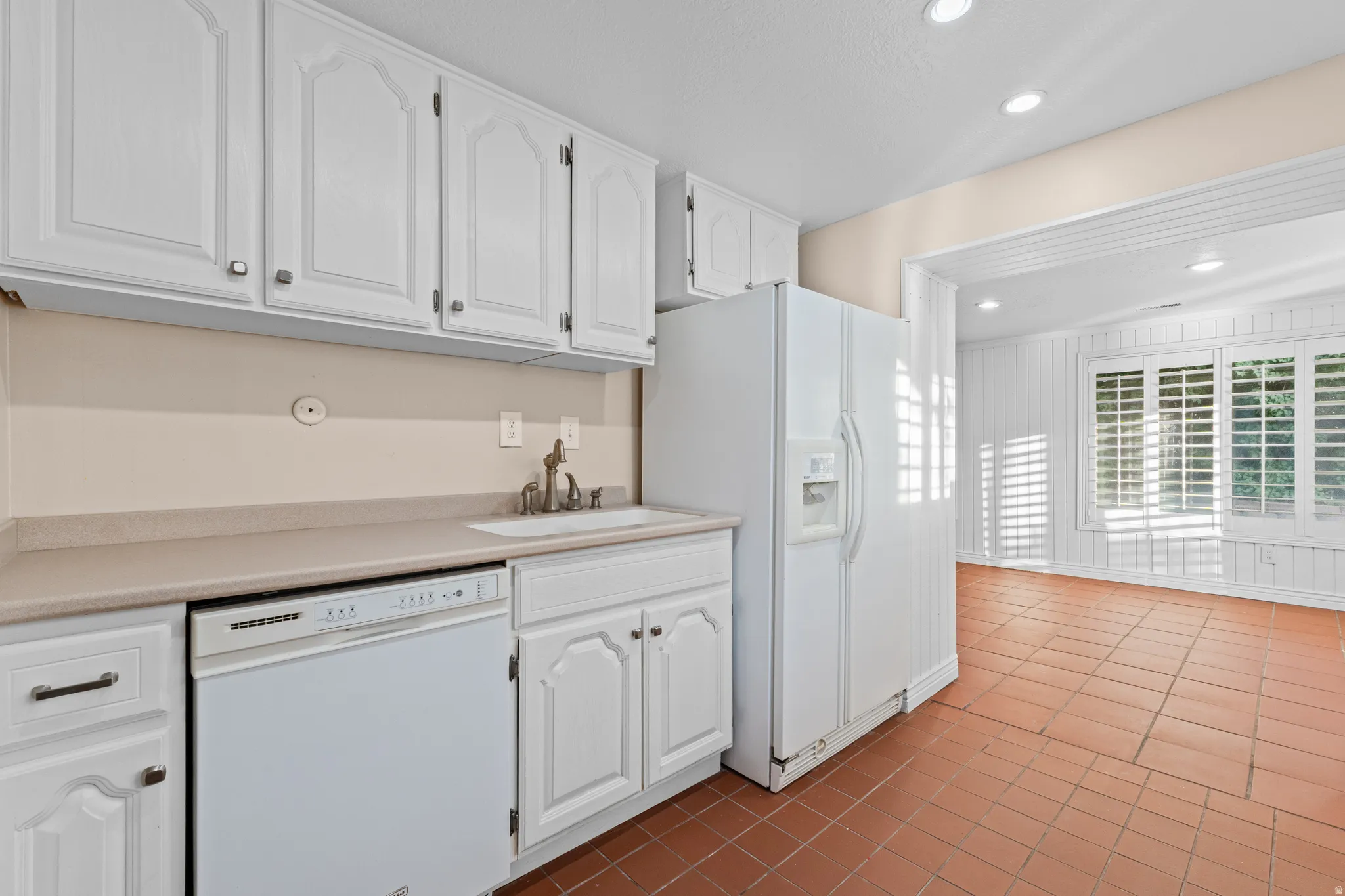 Kitchen area featuring white cabinetry, light countertops, and a white dishwasher