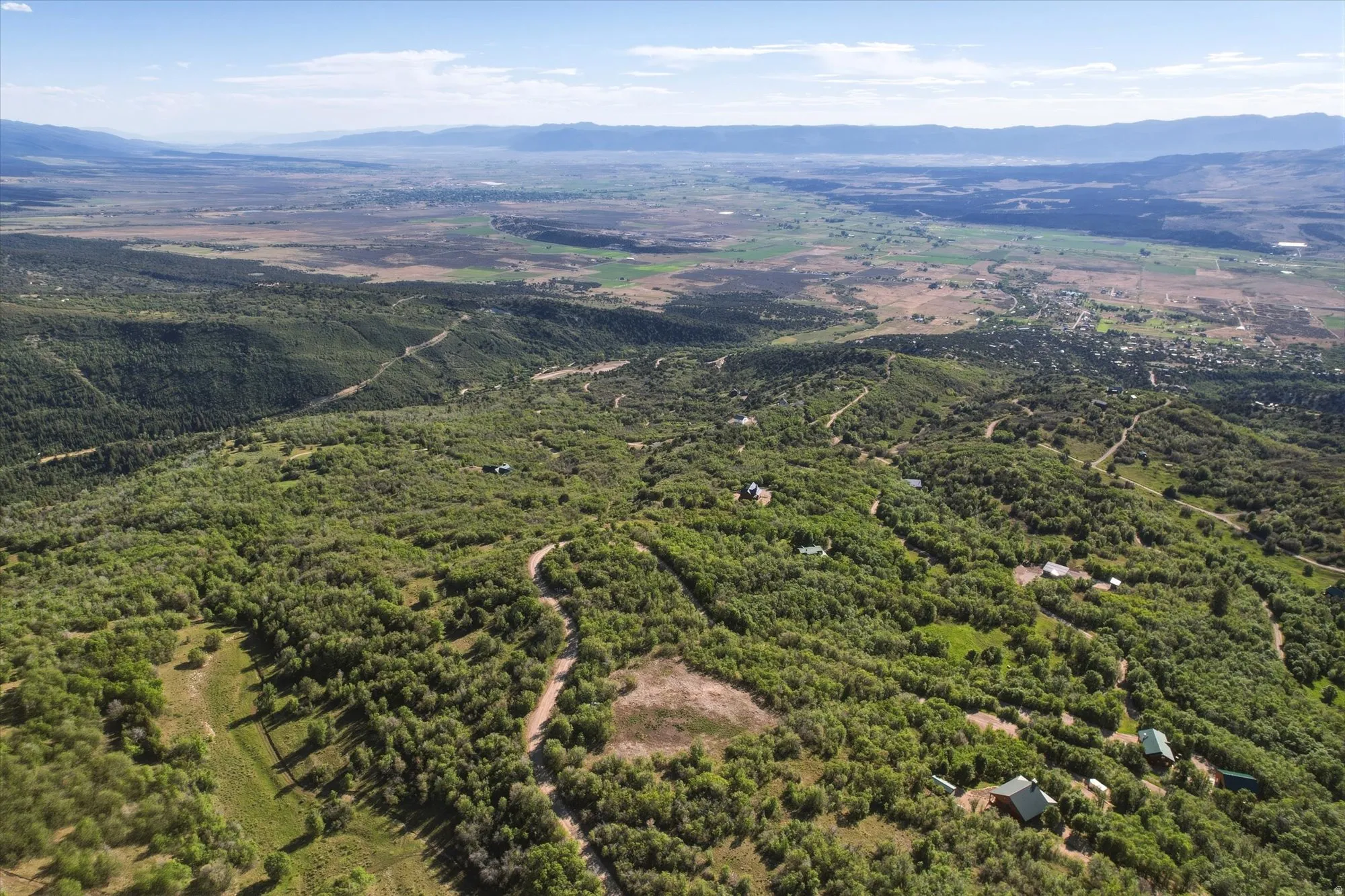 Expansive aerial landscape featuring extensive natural tree coverage, distant mountains ranges, and scattered residential properties throughout the terrain