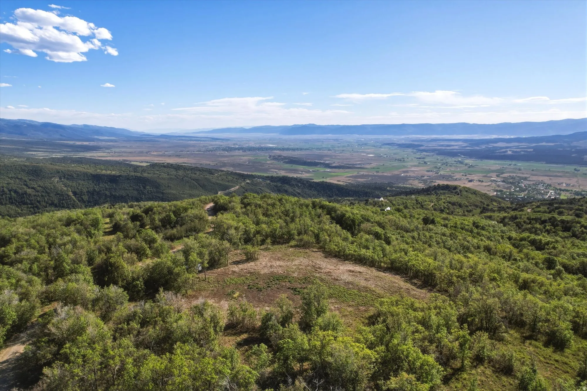 Expansive mountain property featuring mature foliage, a clear building site, and distant valley vistas