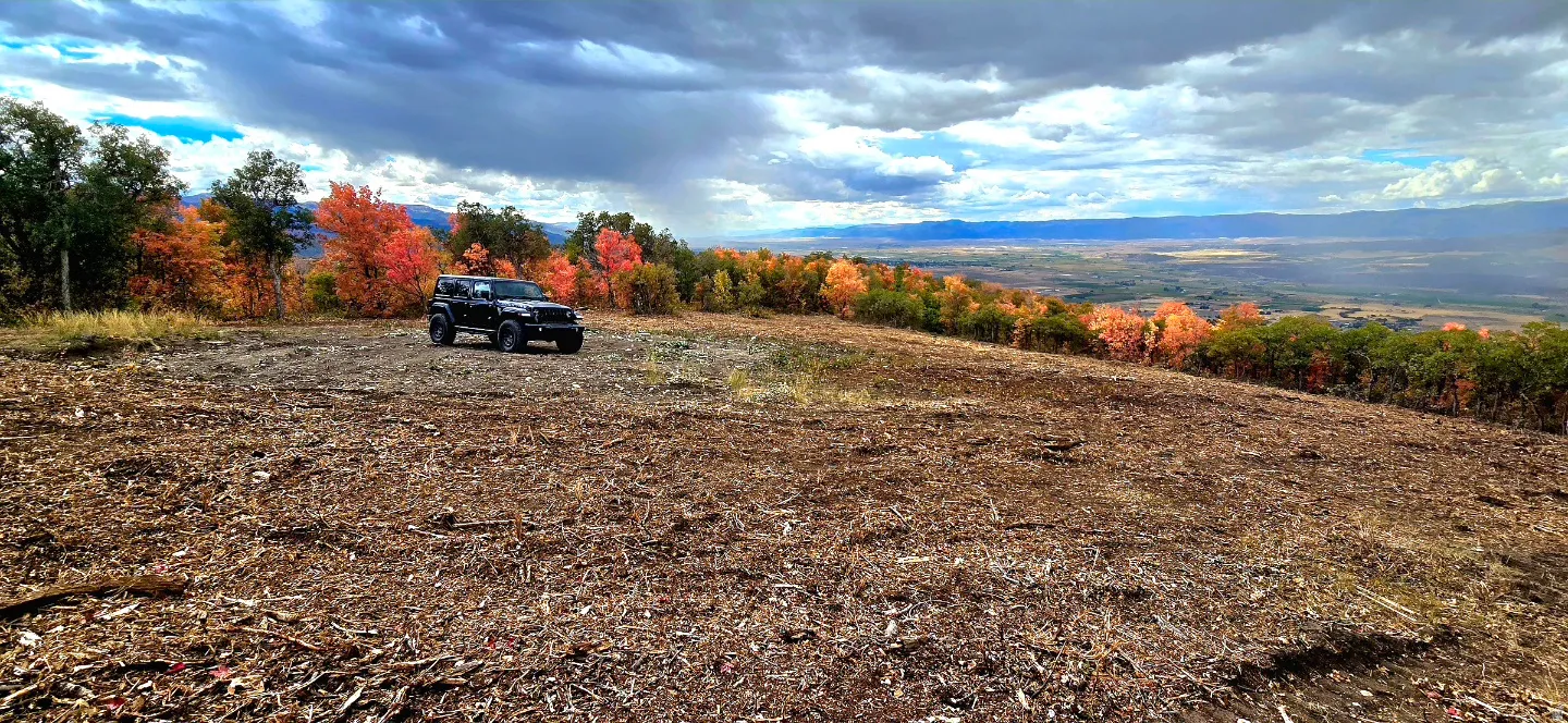 Expansive cleared lot bordered by vibrant autumn foliage and distant mountain ranges