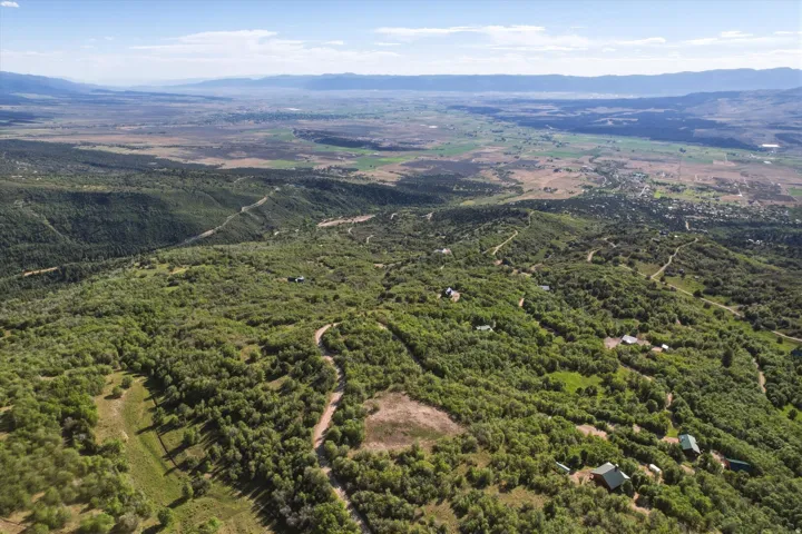 Expansive aerial landscape featuring extensive natural tree coverage, distant mountains ranges, and scattered residential properties throughout the terrain