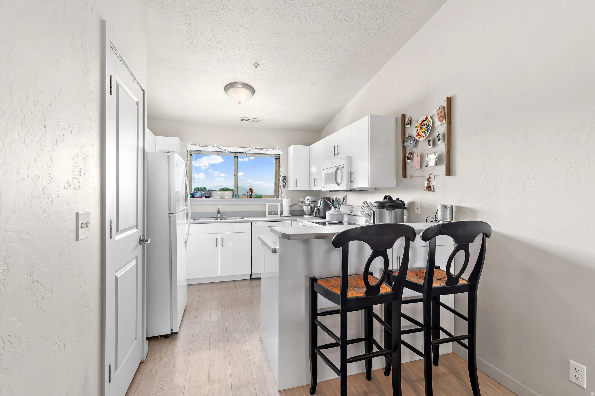 Bright kitchen featuring white cabinetry, a counter-height peninsula, wood-finish flooring, and a large window