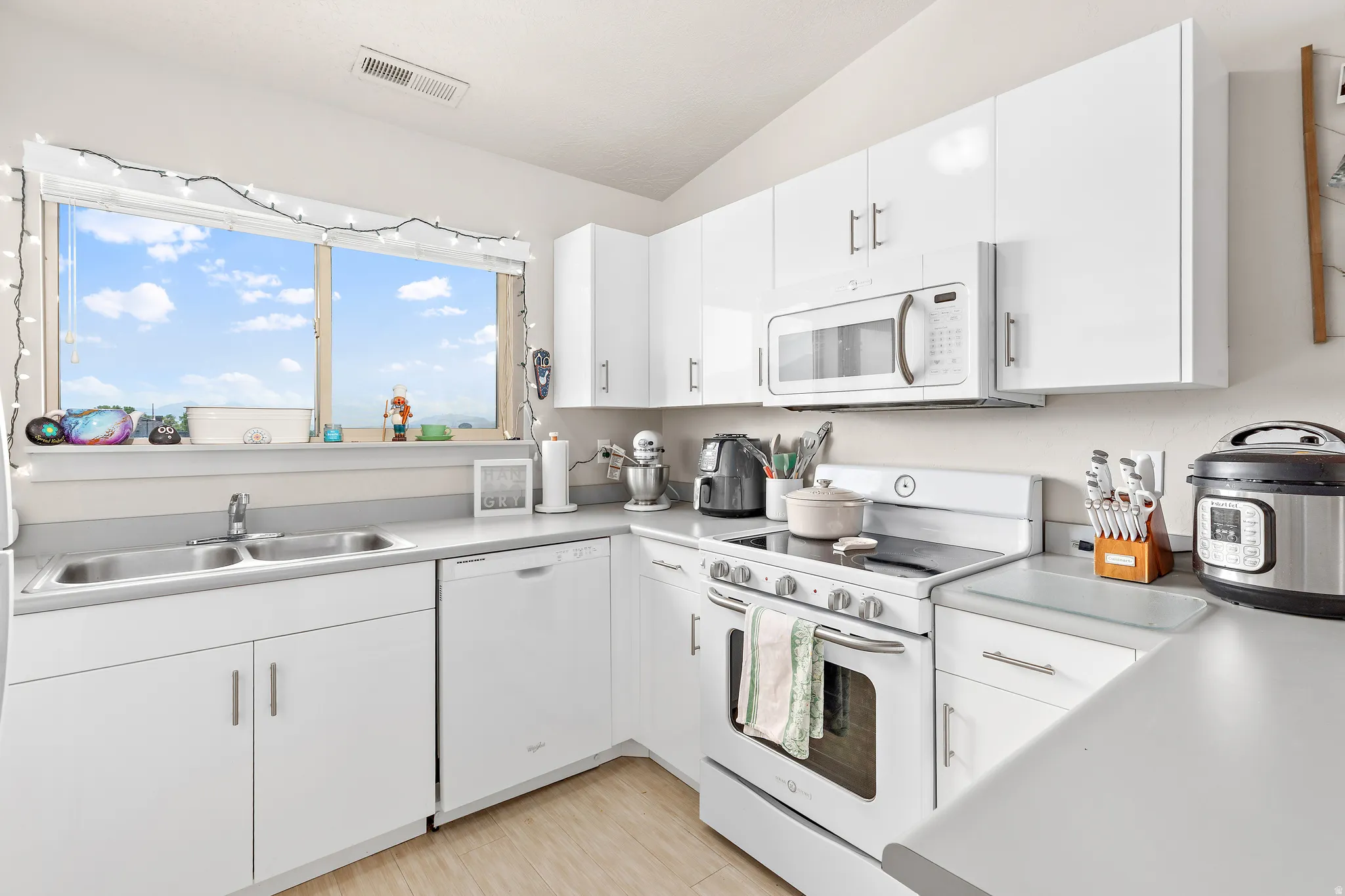 Kitchen featuring white cabinetry, light countertops, a double basin stainless steel sink, and a four-burner electric range with an overhead microwave