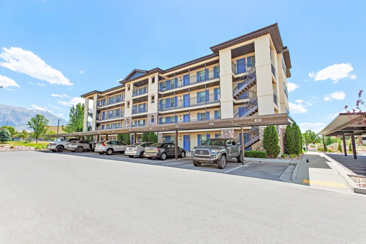 Multi-story building featuring covered parking, exterior balconies with blue railings, and a prominent exterior staircase