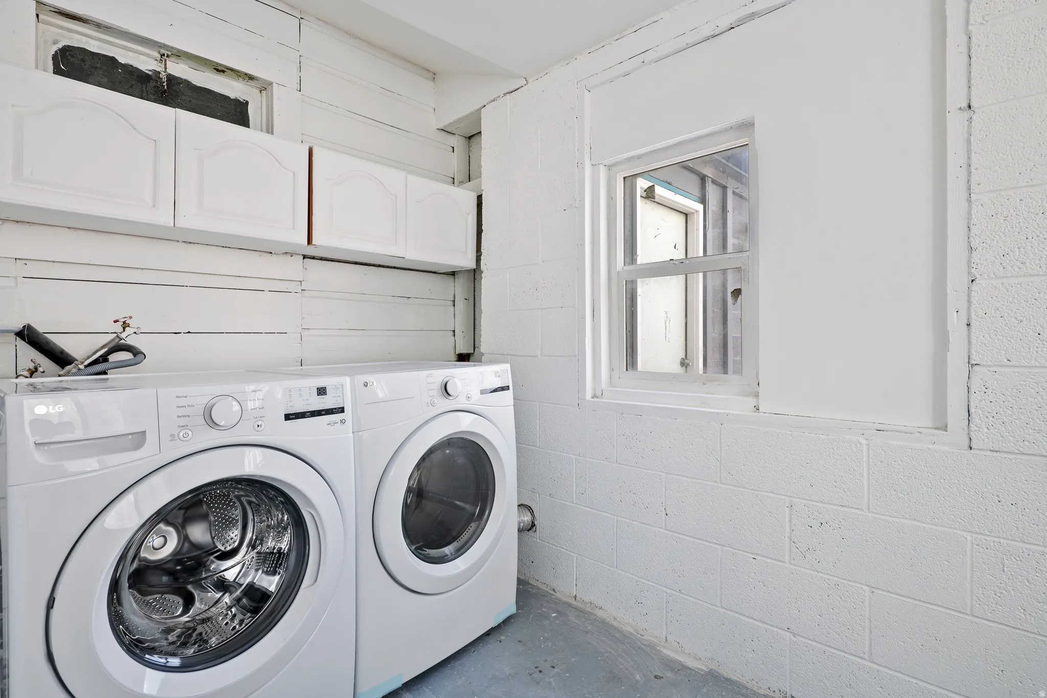 Dedicated laundry area featuring a white front-load washer and dryer set, white upper cabinetry, and a white-framed window