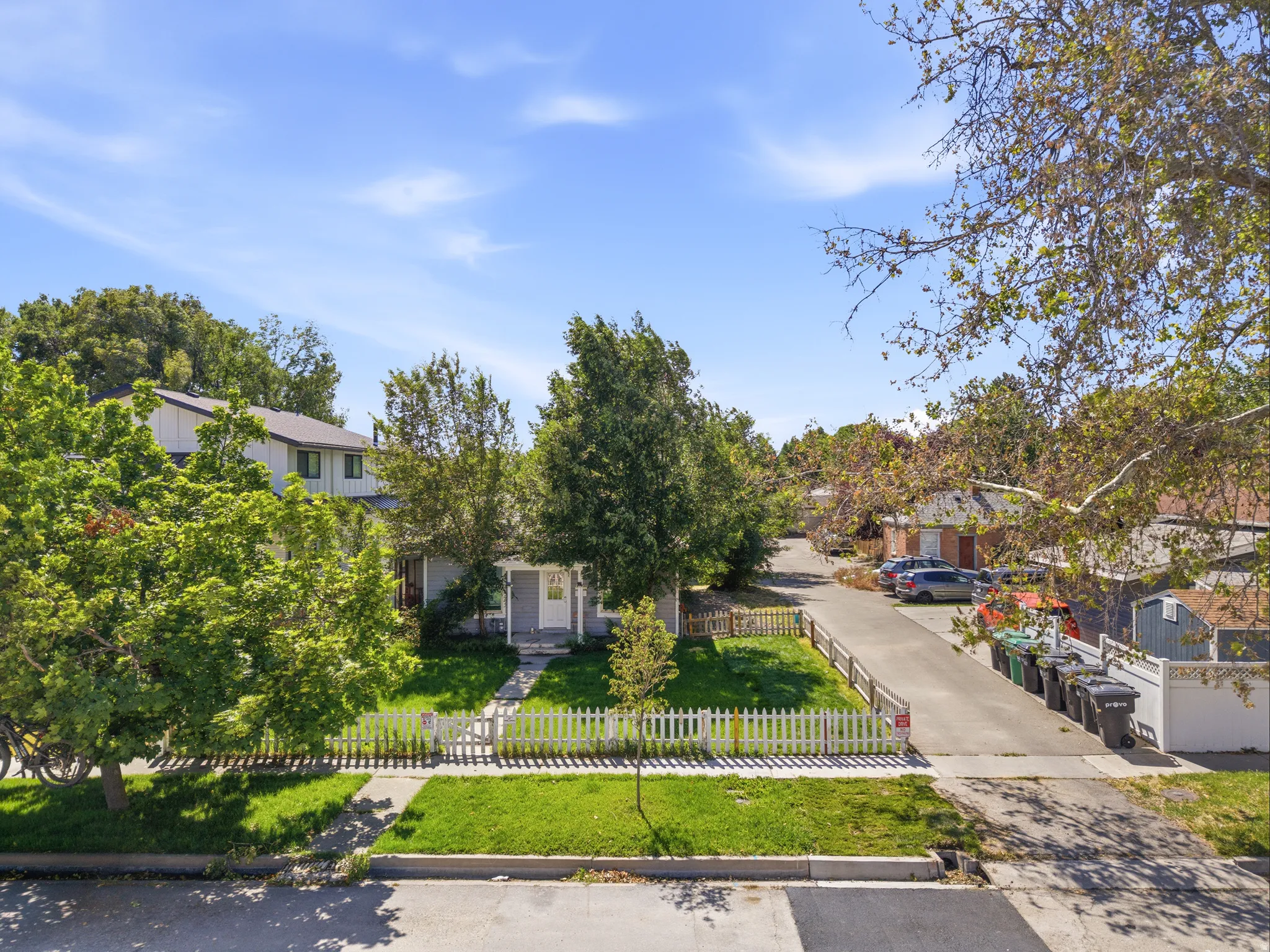 Cottage-style residence with a white picket fence, a manicured front lawn, and mature trees